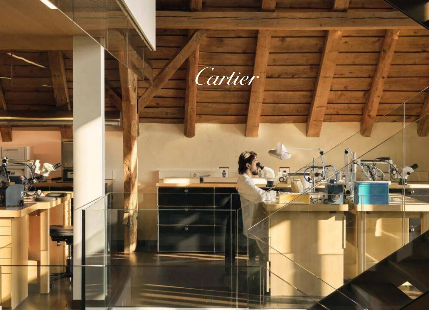 A watchmaker at a bench under the wooden beams of a Cartier manufacture atelier.