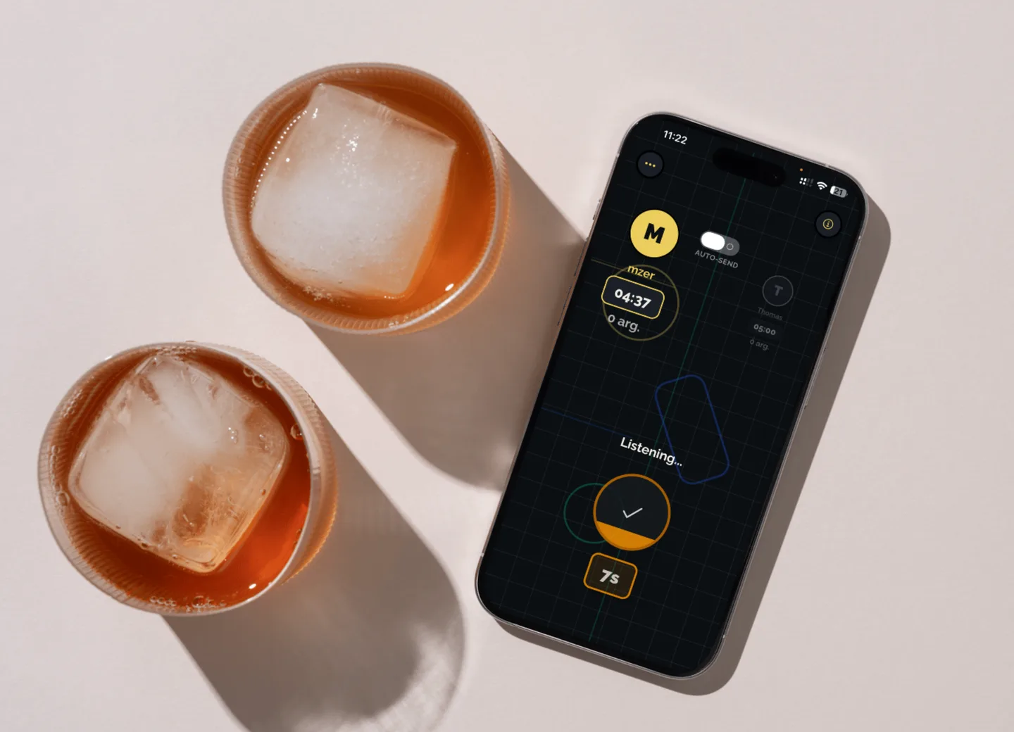 An iPhone lying on a table between two drinks, showing the local duel screen listening to a speaker.
