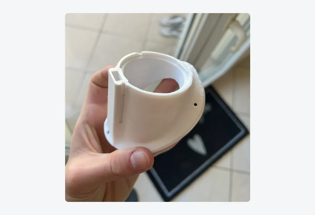 The printed holder held in one hand: white FDM plastic, visible print lines, the rail on the left side and two small drilled holes on the body.